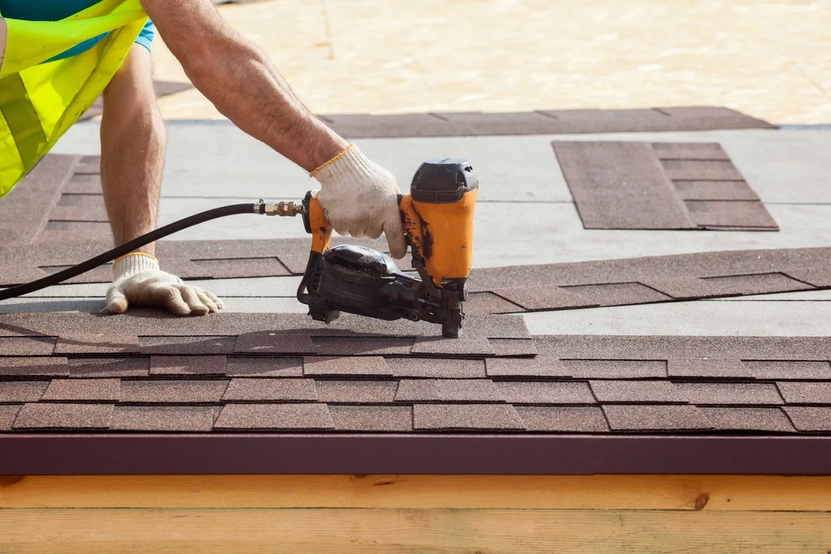 Person using a nail gun to install roofing shingles.