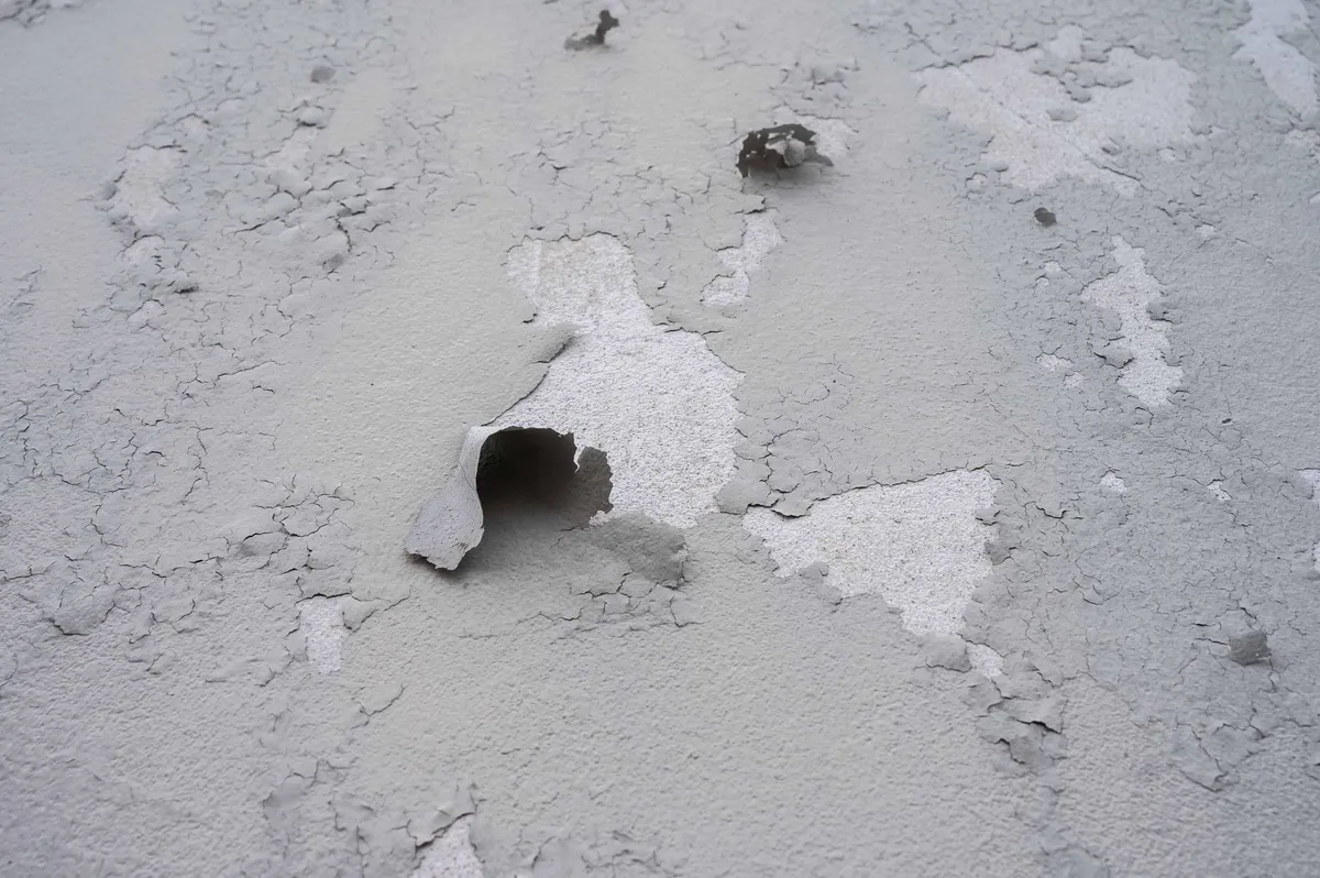 Mur en stuc gris et écaillé avec des trous révélant du plâtre blanc en dessous.