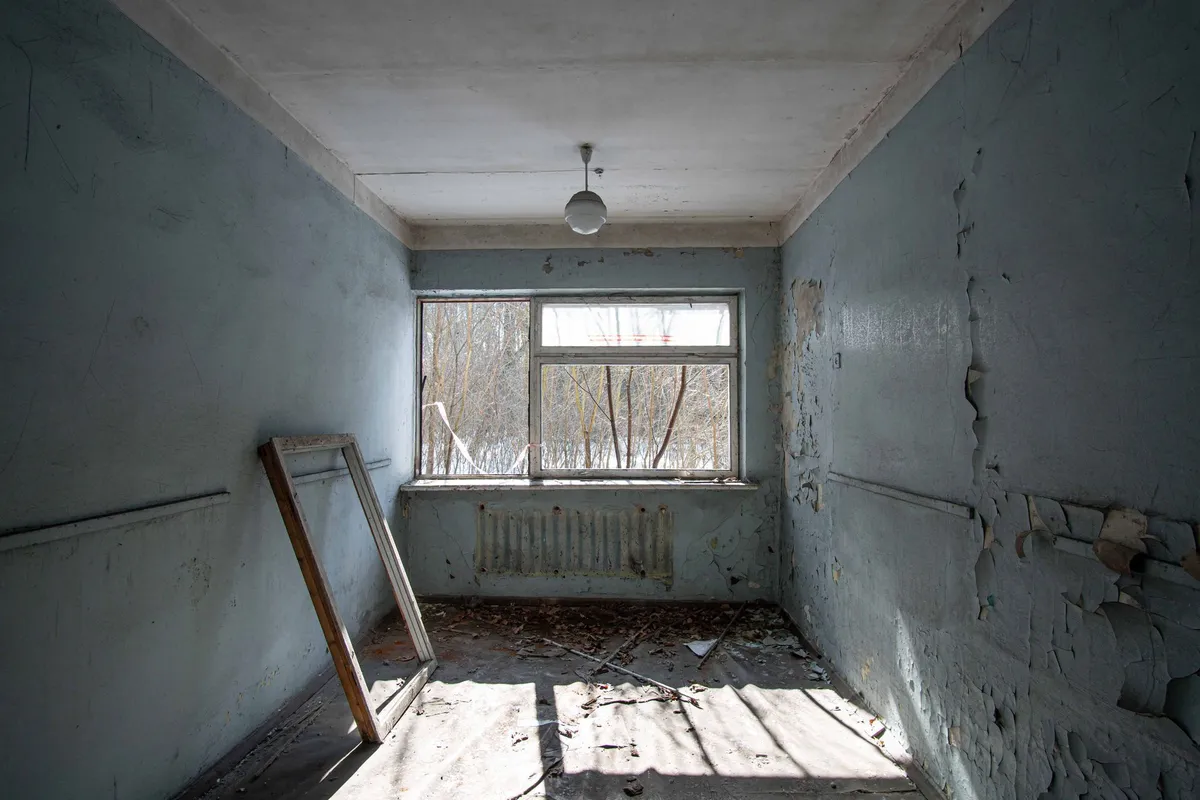 Dilapidated room with peeling blue paint, window, and debris on the floor.